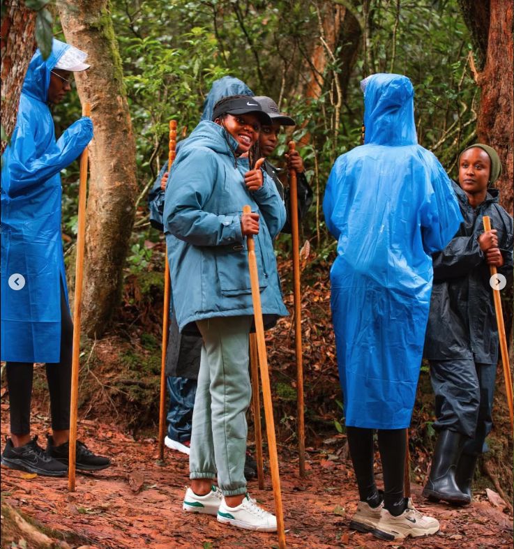 Trekkers in blue raincoats with walking sticks on a red-earth forest path