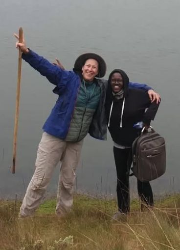 Two smiling trekkers, one holding up a walking stick, on a misty hillside