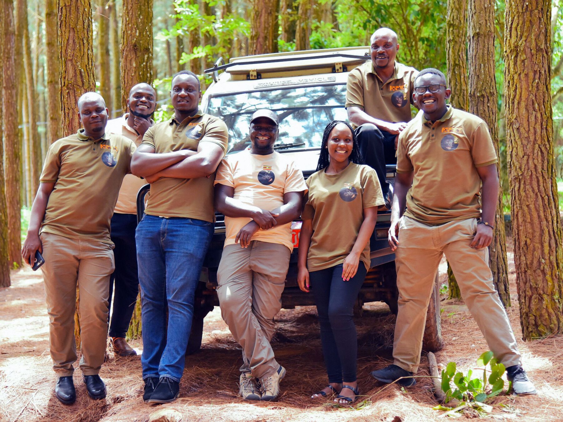 The Iconic Travel Services team in branded uniforms beside a safari vehicle in a forest